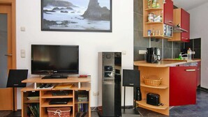 A compact living space with a television, a small refrigerator, a kitchenette, and a dining area. - Doppelhaushaelfte am Hafen von Neuendorf (Neuendorf)