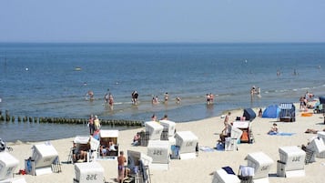 Ein Strand mit Liegestühlen und Sonnenschirmen, einer Seebrücke und Menschen, die schwimmen und sonnenbaden.