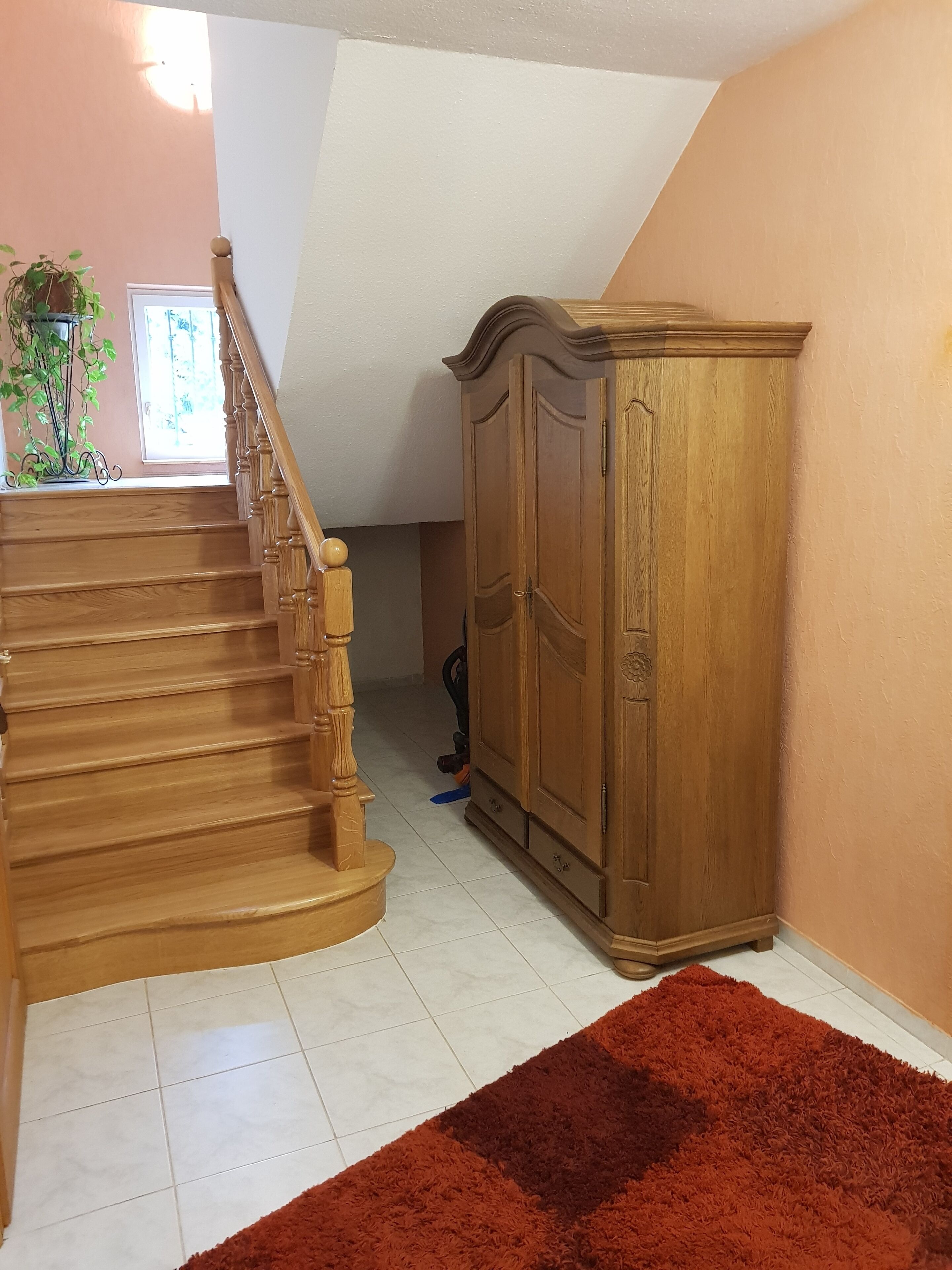 Una escalera de madera con barandilla, que conduce a un rellano con un armario de madera y una alfombra roja.