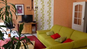 Un salón con sofá amarillo, televisor, candelabro y puerta con paneles de vidrio.