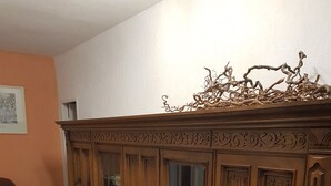 Un mueble de madera con puertas de cristal, un sofá marrón y una alfombra roja en una habitación con paredes blancas y suelo de baldosas.