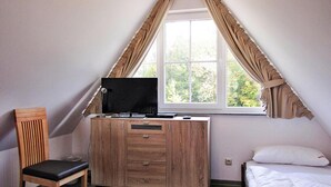 A bedroom with a sloped ceiling, a wooden desk with a TV, a chair, and a bed with white bedding. - Ferienhaus Nachtigall, Glowe (Glowe)