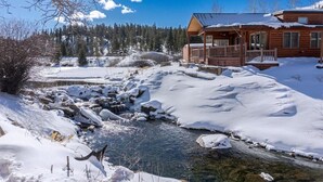 Une cabane en rondins dotée d’un porche donnant sur un ruisseau enneigé.