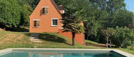 A house with a swimming pool, surrounded by greenery and trees.