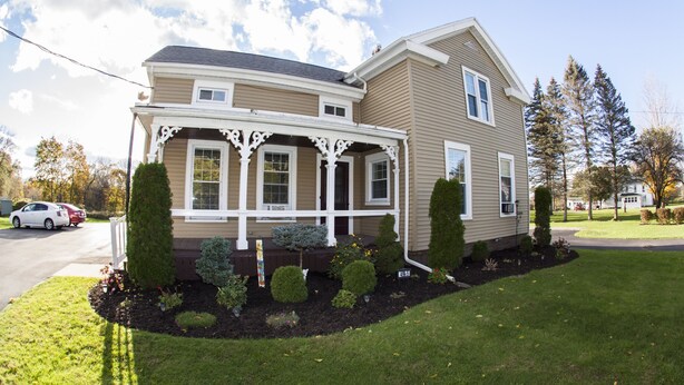 A two-story house with a covered porch, a well-maintained lawn, and a driveway with cars parked. - Comfortable place to work, Priced per-person rate (Vernon)