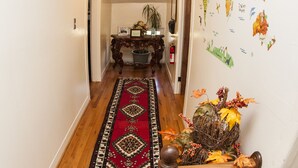 A hallway with a wooden floor, a red patterned rug, a decorative plant, and a wall map. - Comfortable place to work, Priced per-person rate (Vernon)