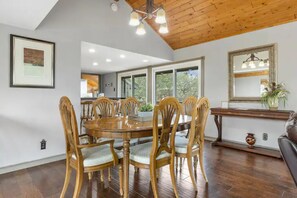 A dining area with a wooden table and chairs, a chandelier, and a large window.