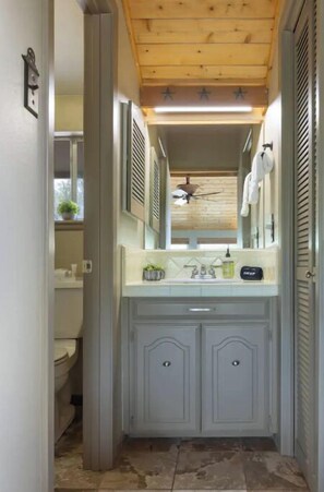 A narrow bathroom with a wooden ceiling, a white sink with a mirror above it, and two cabinets below.
