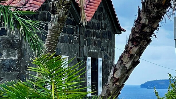 A stone building with a red roof, palm trees, and a view of the sea.