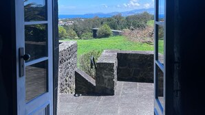 An open door leading to a stone patio with a view of a green landscape and distant hills.