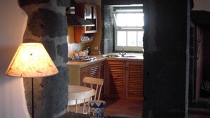 A kitchen with a stone pillar, wooden cabinets, a window, and a table with a chair.