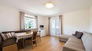 A cozy living room with a sofa, a dining table with chairs, and a TV on a small cabinet. - Apartment in Dorf Tirol near Tirol Castle (Dorf Tirol)