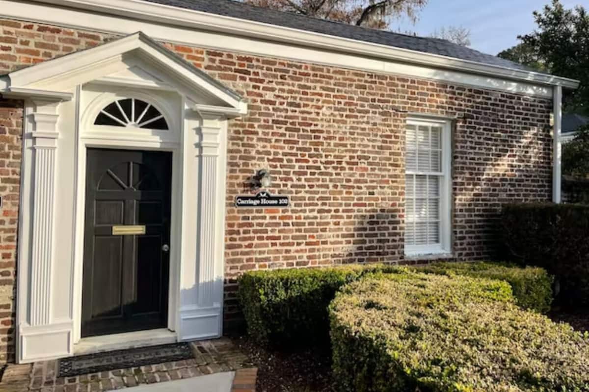 A brick building with a black door and a sign that reads "Carriage House 123".