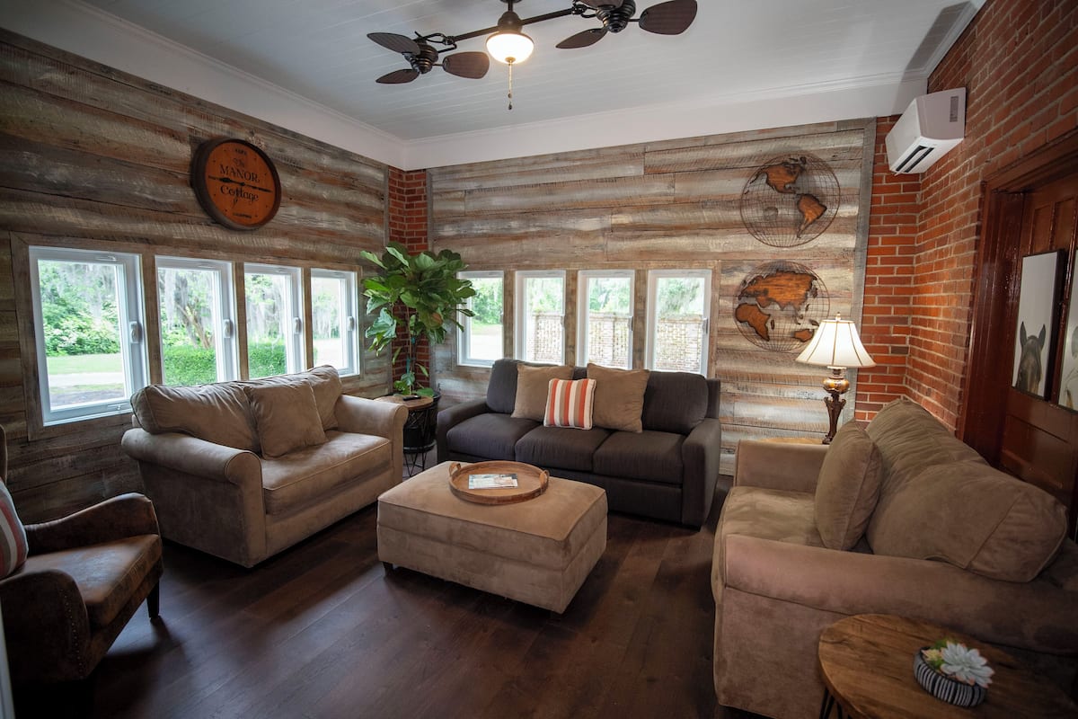 A cozy living room with wooden walls, a ceiling fan, and a large window overlooking greenery.