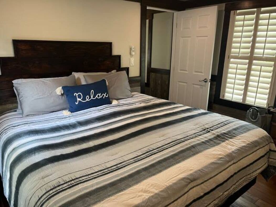 Una cama con ropa de cama a rayas y una almohada con la palabra 'Relax'.