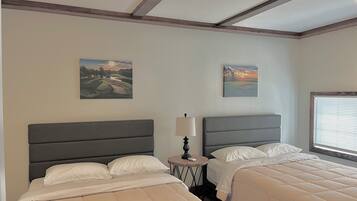 A hotel room with two beds, a round table with a lamp, and two paintings on the walls.