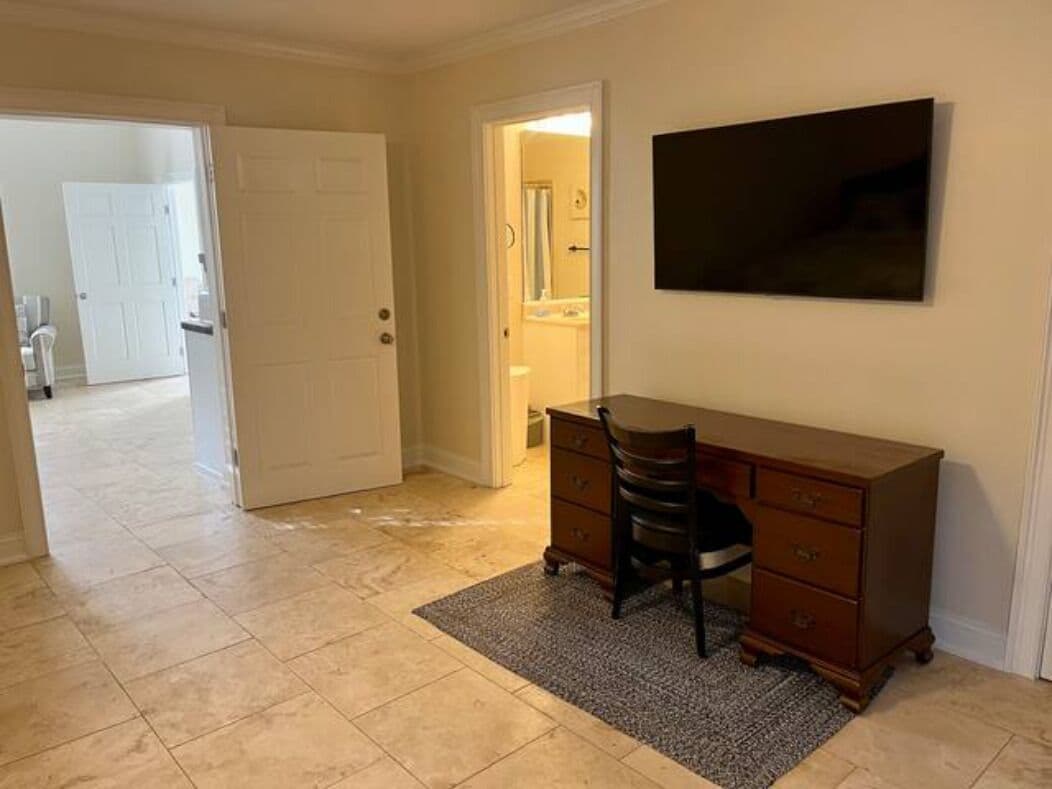 A room with a desk, chair, and a flat-screen TV mounted on the wall.