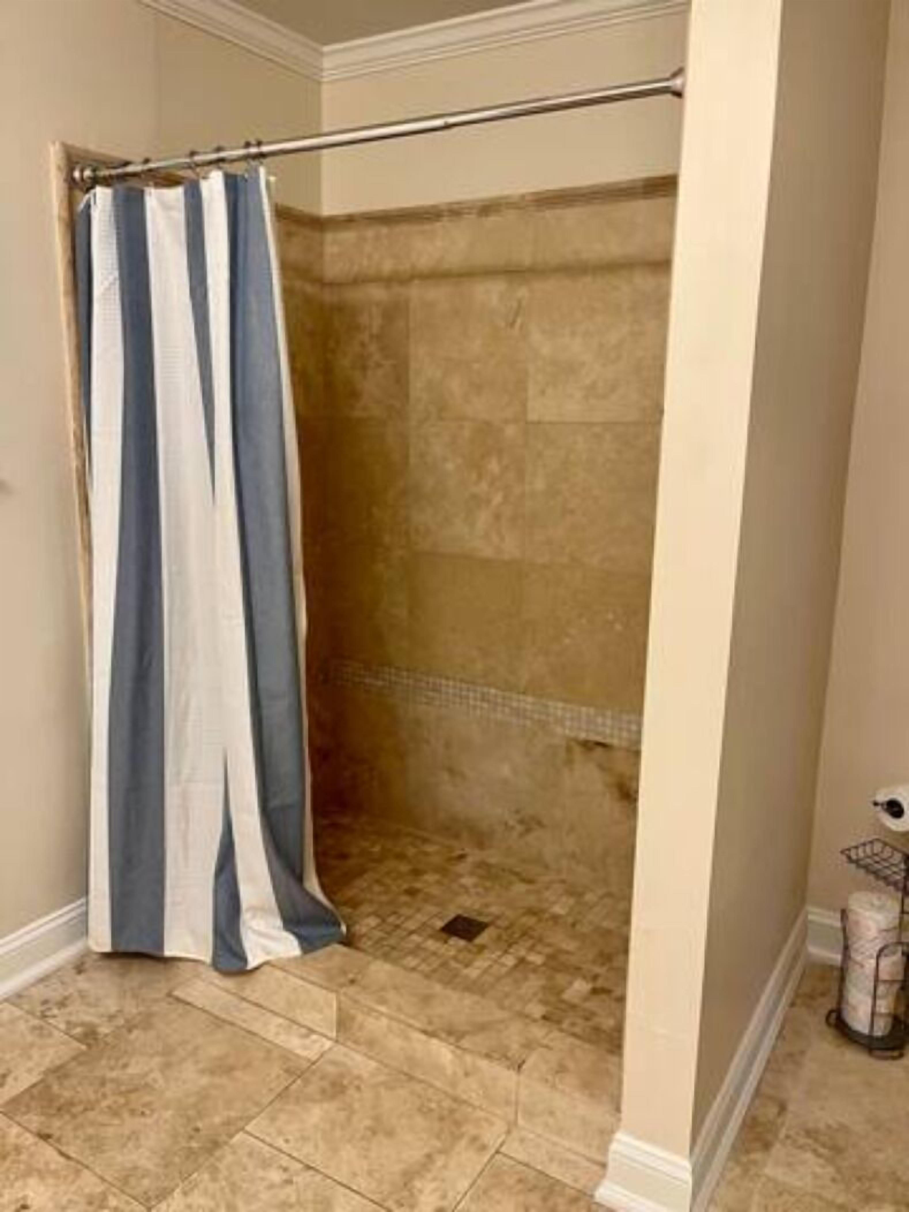 A bathroom with a shower area, tiled floor, and a towel rack.