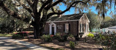 A brick building with a sign reading "Brick House Pub" surrounded by large trees and a well-maintained garden.