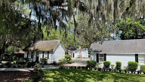 A white building with a gabled roof, surrounded by lush greenery and trees with hanging moss.