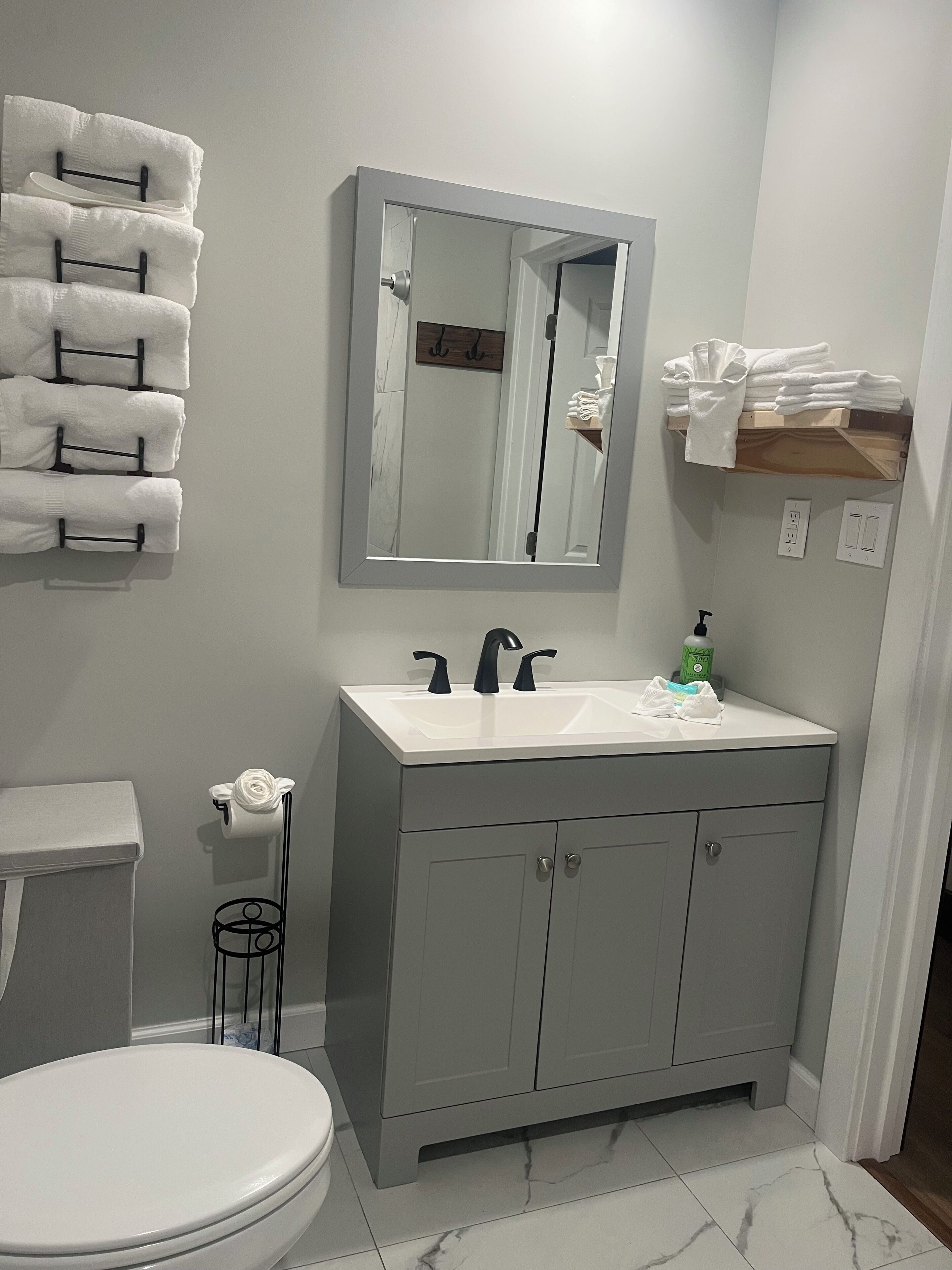 Ein Badezimmer mit Toilette, Waschbecken, Spiegel, Handtuchhalter und einem Regal mit gefalteten Handtüchern.