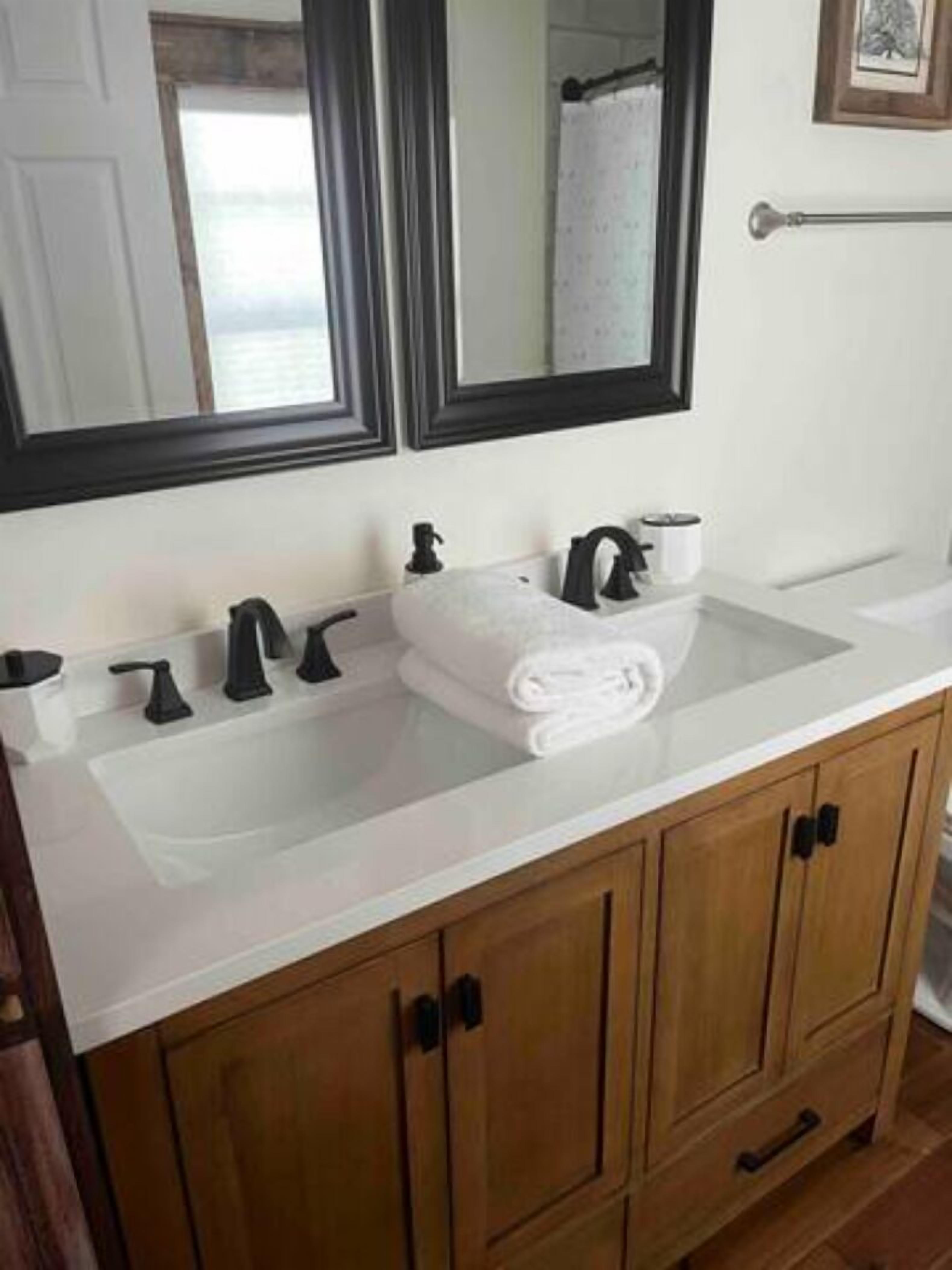 Un baño con lavamanos blanco, dos grifos negros, una toalla y armarios de madera.
