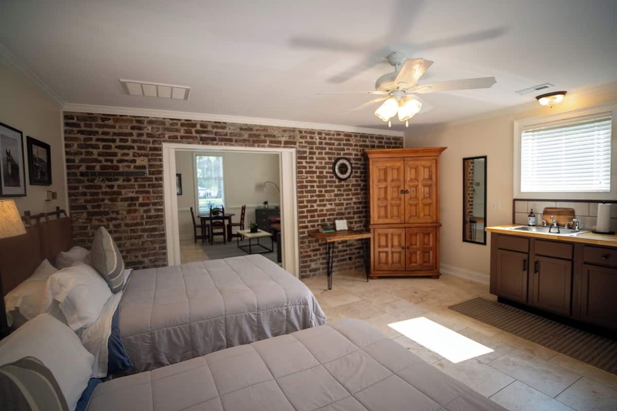 A bedroom with two beds, a wooden wardrobe, a ceiling fan, and a brick wall.