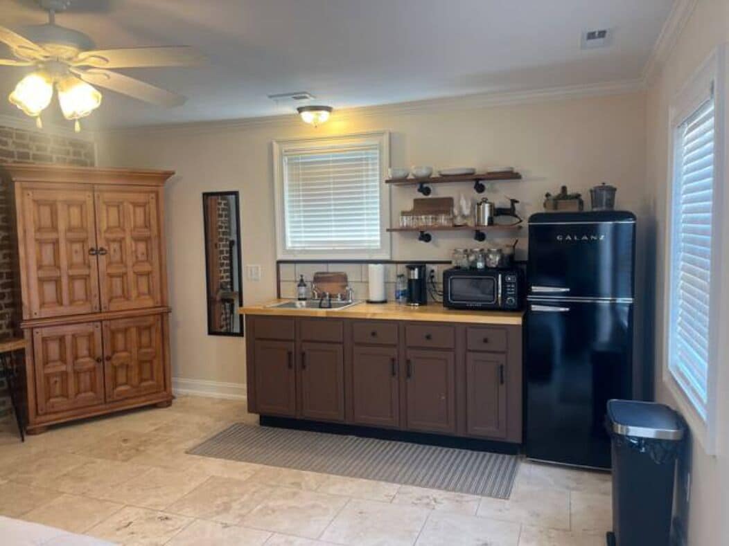 A kitchen with a black refrigerator, wooden cabinets, a microwave, and a ceiling fan.