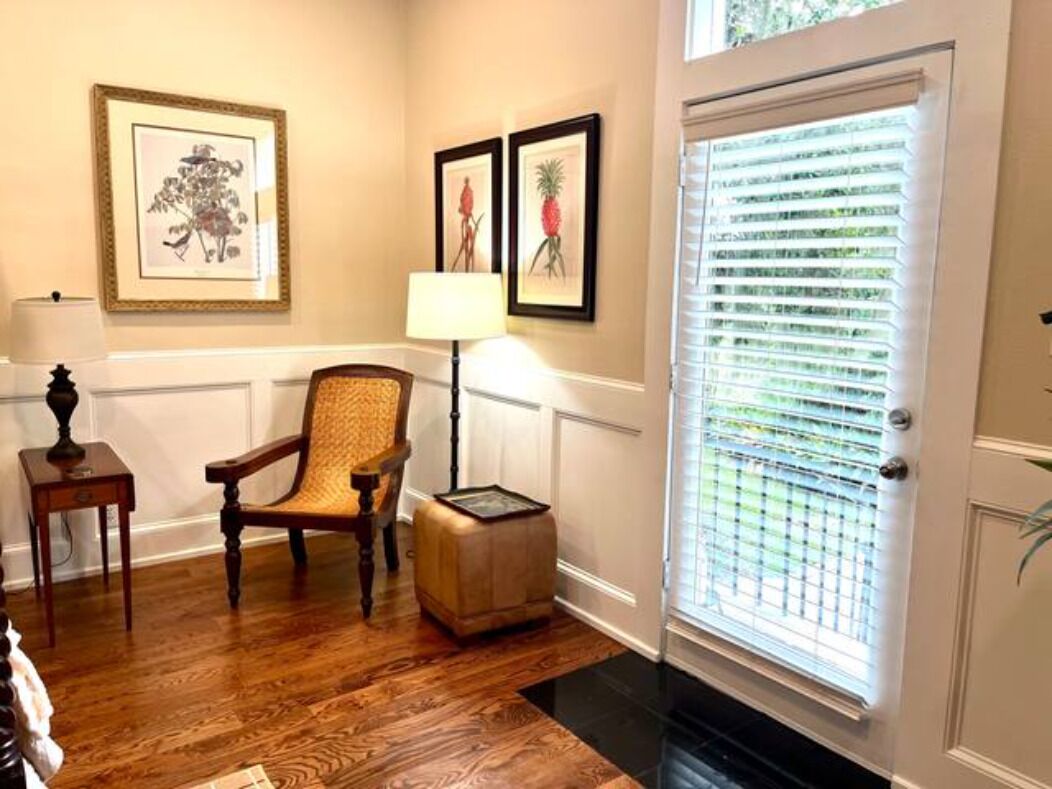 A room with hardwood flooring, a chair, a lamp, and a door with blinds.