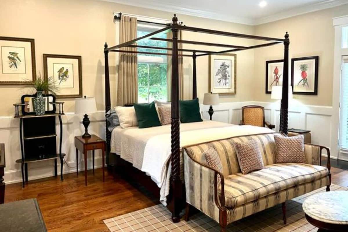 A four-poster canopy bed with a wooden frame, a sofa with patterned cushions, and framed artwork on the walls.