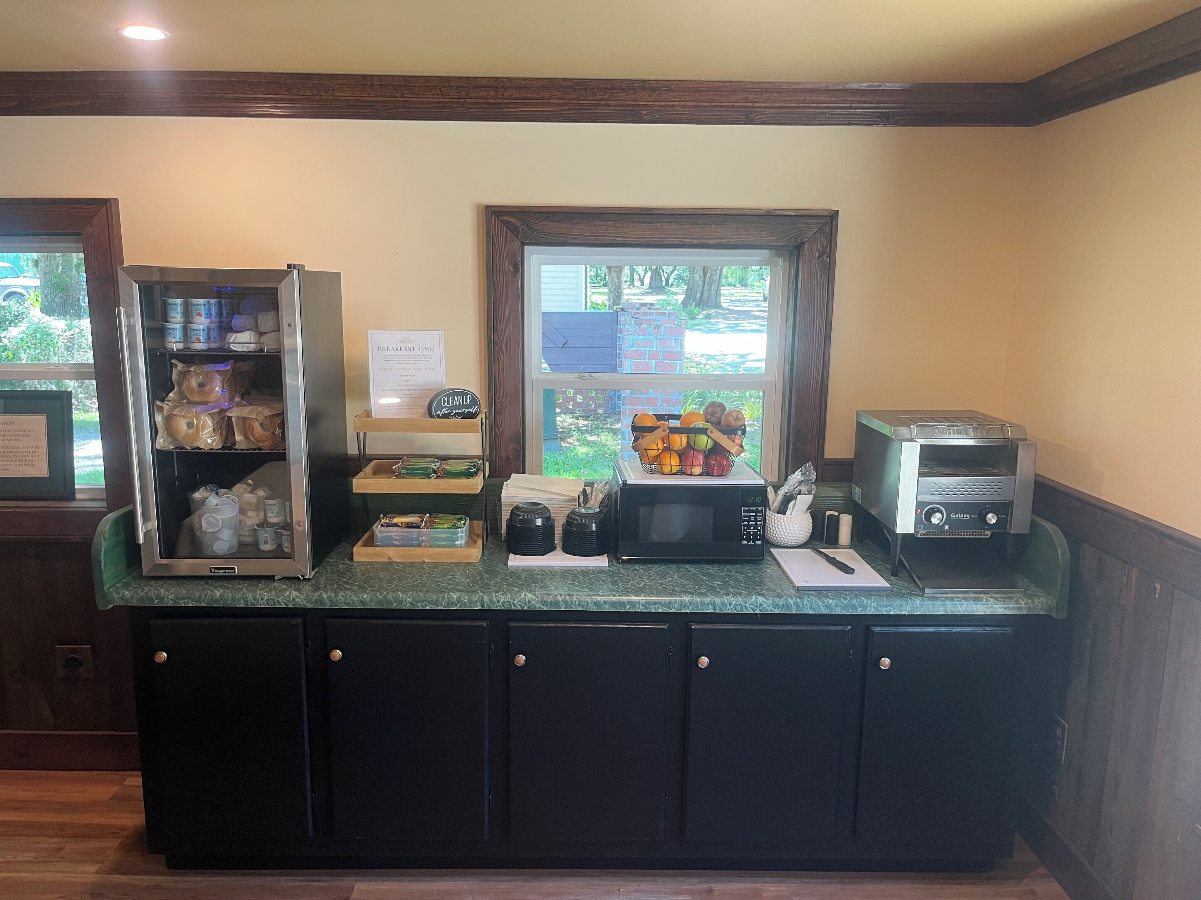 A breakfast bar with a refrigerator, microwave, and a window with a view of trees.