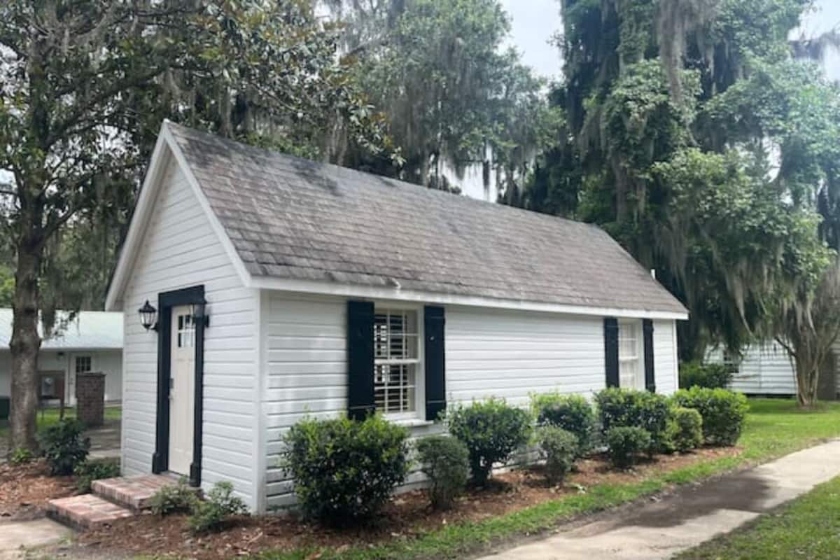 A small white building with a gabled roof, a front door, and a window with shutters.
