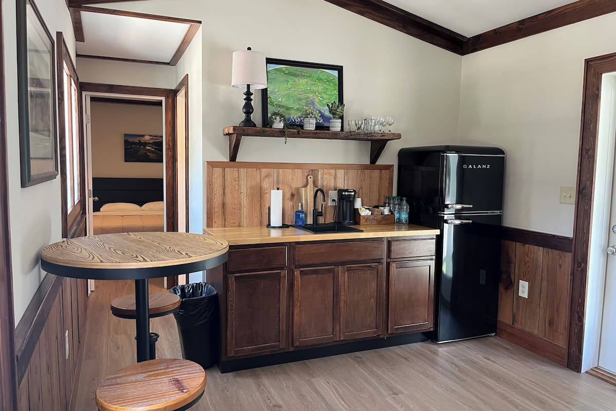 A compact kitchen with wooden cabinets, a black refrigerator, a coffee bar, and a small round table.