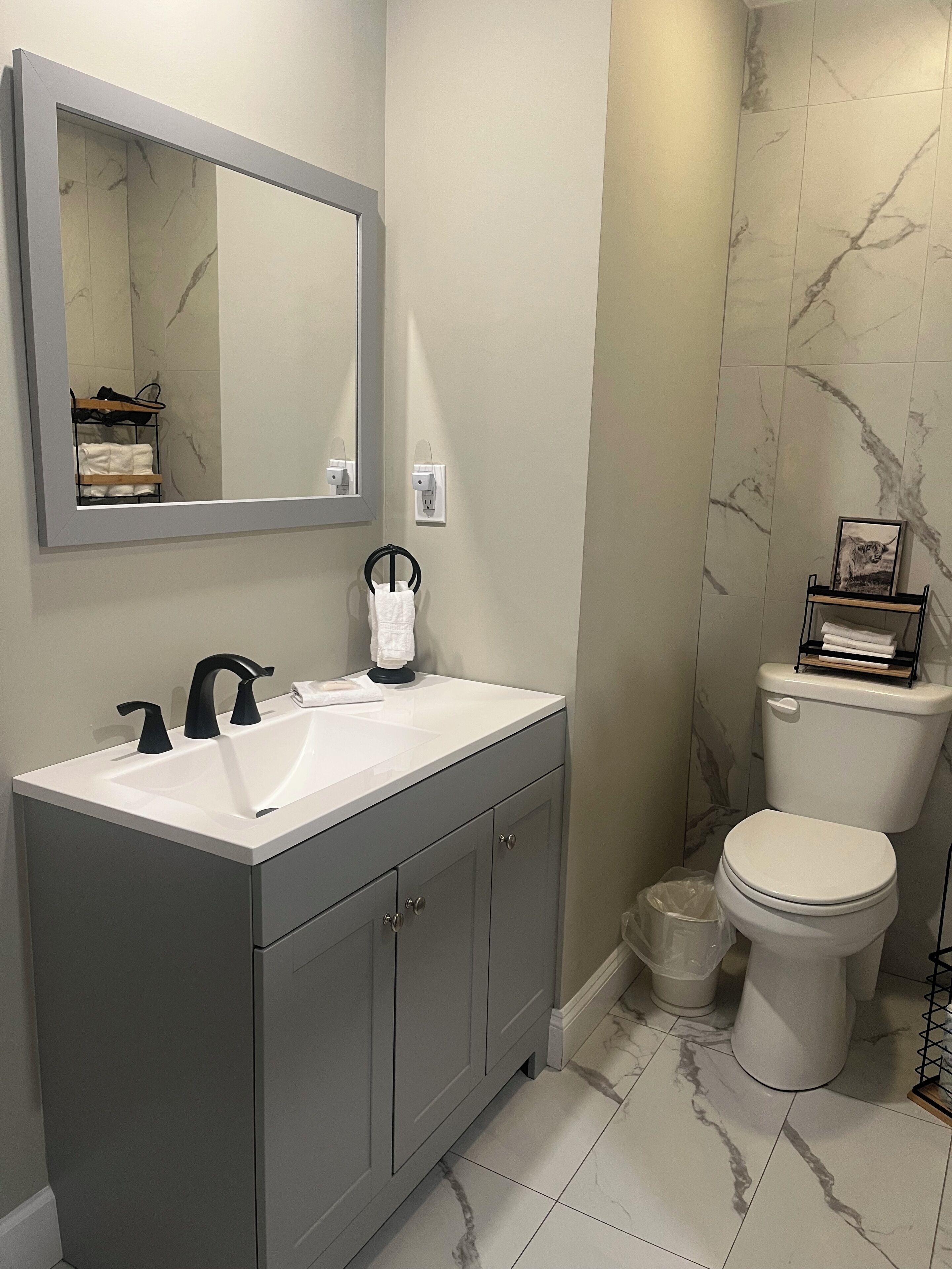 A modern bathroom with a white sink, black faucets, a large mirror, and a toilet.