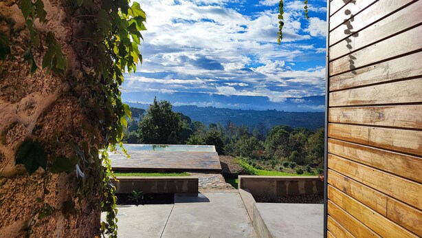 Un patio al aire libre con suelo de concreto, paredes de madera y vista a un paisaje montañoso bajo un cielo parcialmente nublado.