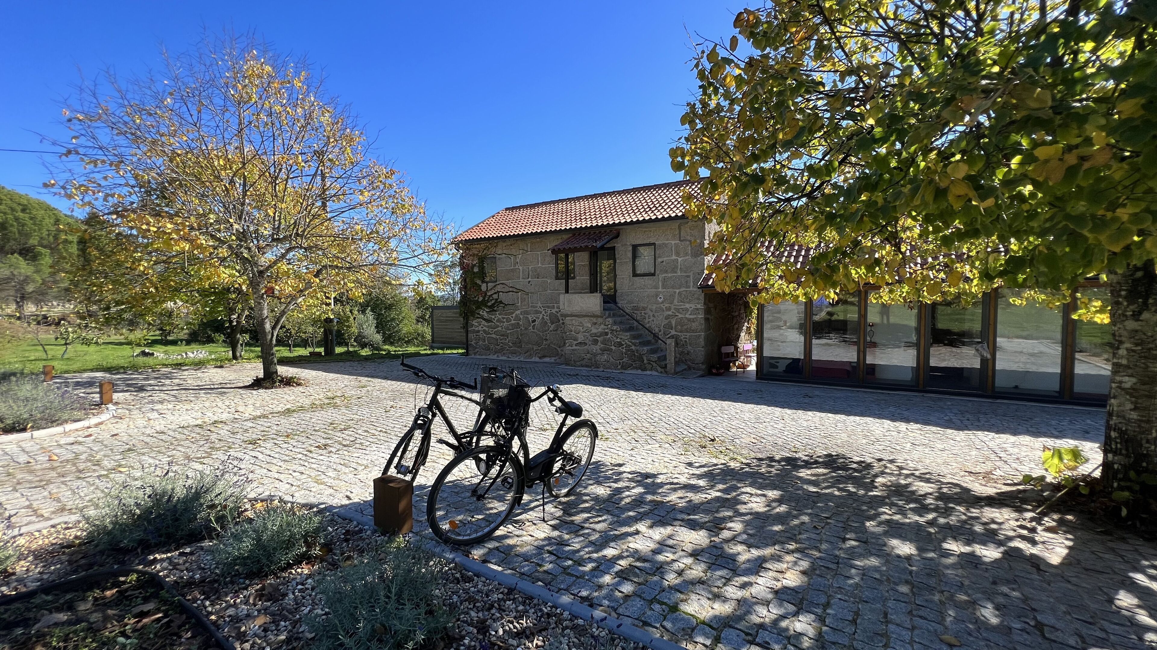 A stone building with a tiled roof, a cobblestone driveway, and a bicycle parked in front.