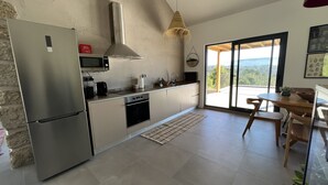 Una cocina moderna con un refrigerador de acero inoxidable, microondas y estufa, un ventanal con vistas, y un comedor con una mesa y sillas de madera.