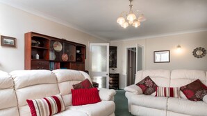 A spacious living room with two white leather sofas, a wooden cabinet, and a chandelier. - A detached, dog-friendly bungalow with a large garden near Abergele (Abergele)