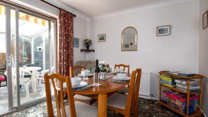 A dining area with a table set for four, surrounded by wooden chairs. A bookshelf filled with books is to the right. - A detached, dog-friendly bungalow with a large garden near Abergele (Abergele)
