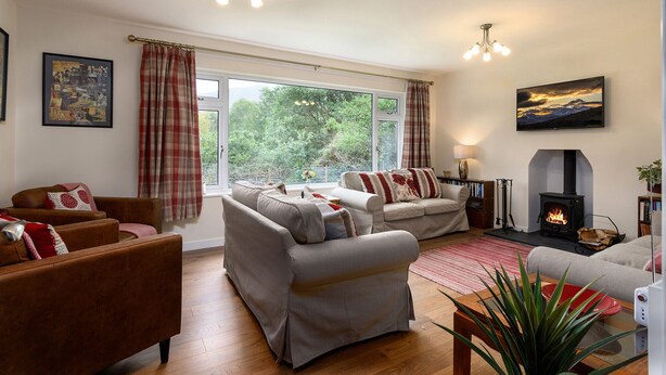 A cozy living room with a fireplace, two sofas, a coffee table, and a large window with curtains. - Cosy family cottage close to Beddgelert and Porthmadog (Porthmadog)