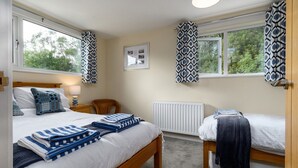 A bedroom with two beds, a wooden headboard, a radiator, and patterned curtains. - Cosy family cottage close to Beddgelert and Porthmadog (Porthmadog)