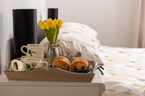 A wooden tray with a mug, tulips, and croissants on a bedside table.