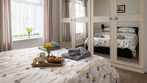 Ein Schlafzimmer mit einem Bett, einem Nachttisch mit Blumenvase und einem Tablett mit Gebäck und Tassen.