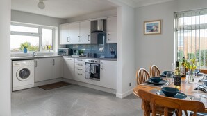 Eine moderne Küche mit weißen Schränken, einem eingebauten Backofen und einem Essbereich mit Tisch für zwei Personen.