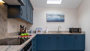 A modern kitchen with blue cabinets, a granite countertop, a sink, a microwave, and a painting of a coastal scene.