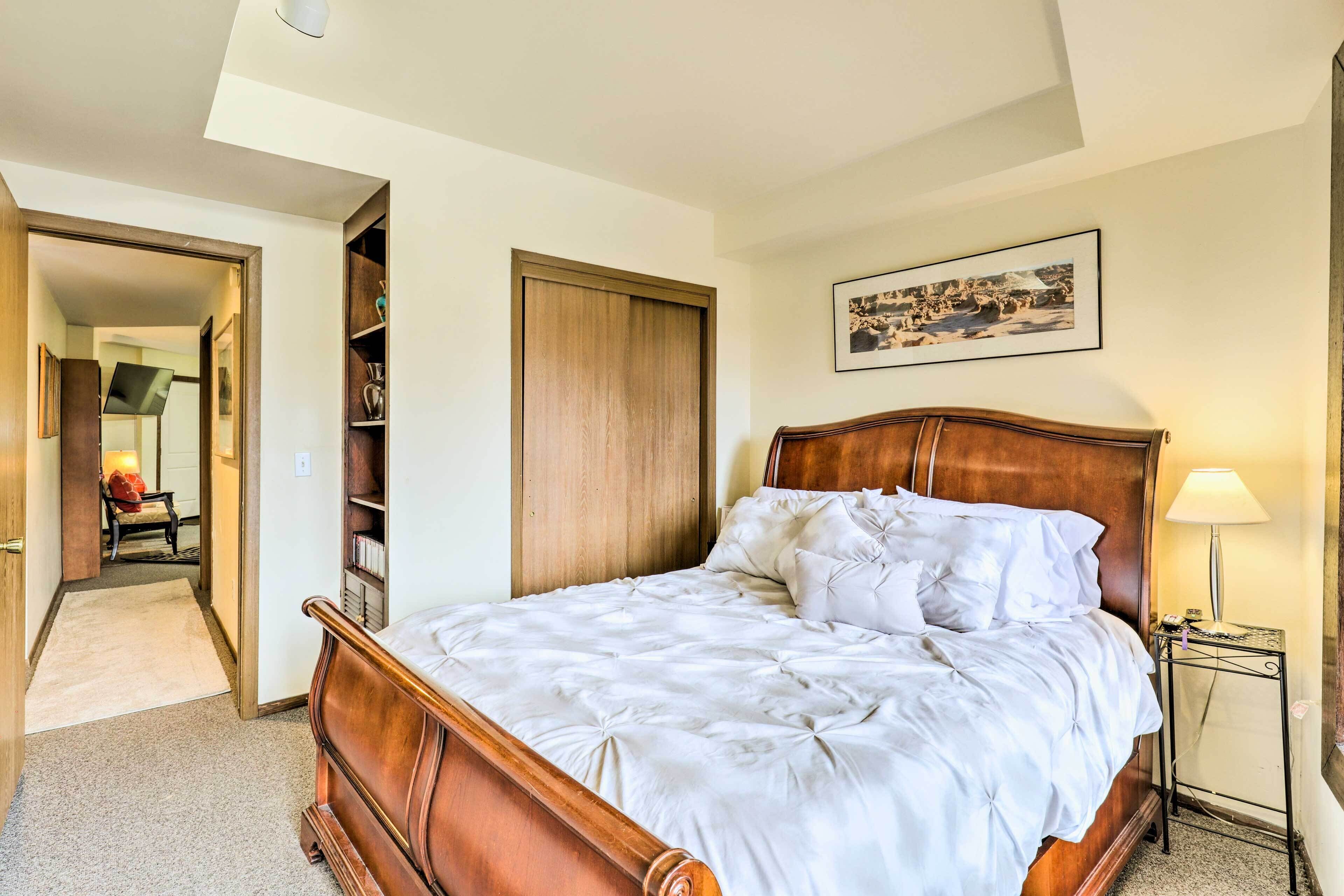 Une chambre à coucher avec un lit en bois, une table de chevet, une commode, un tableau encadré au mur et un placard.