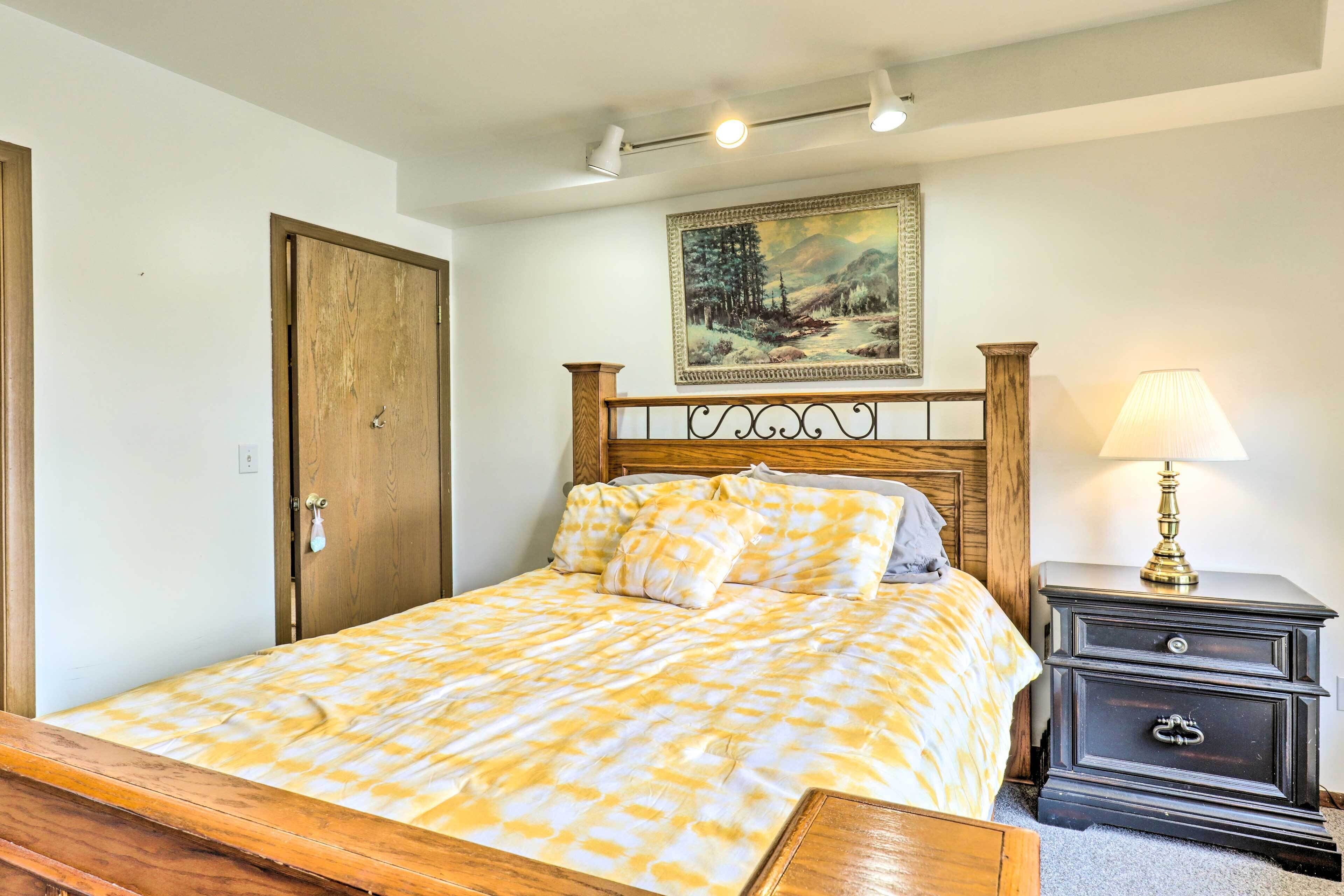 A bedroom with a bed, a nightstand, a lamp, a door, and a painting on the wall.