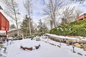 Ein verschneiter Außenbereich mit Holzterrasse, Steinmauer und schneebedeckten Sitzgelegenheiten.