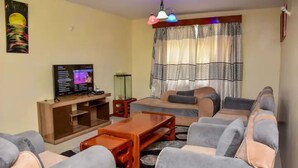 Una sala de estar con un sofá, sillones, una mesa de centro, un televisor y una cortina estampada.