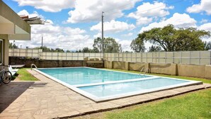 Una piscina rectangular con un borde de piedra, una bicicleta y un edificio de techo plano al fondo.